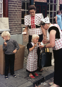 845727 Afbeelding van twee in klederdracht gestoken vrouwen en kinderen die smullen van een portie poffertjes in de ...